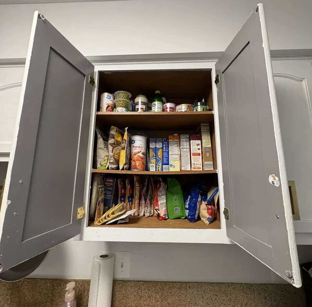 Kitchen pantry cabinet after organizing, with canned goods and boxed food grouped by category on each shelf