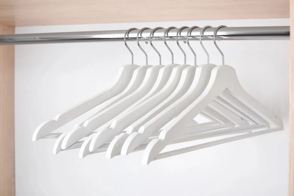 Matching white hangers evenly spaced on a closet rod